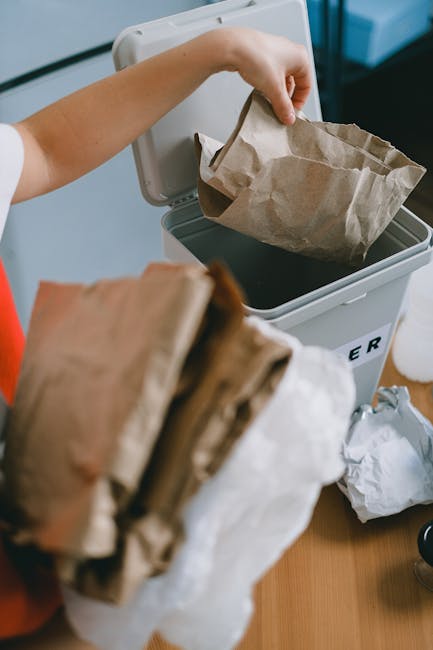 The image depicts an outdoor area used for rubbish disposal, featuring several large stacks of flattened cardboard boxes with printed labels for fresh fruits, arranged in a pile on the ground. These c